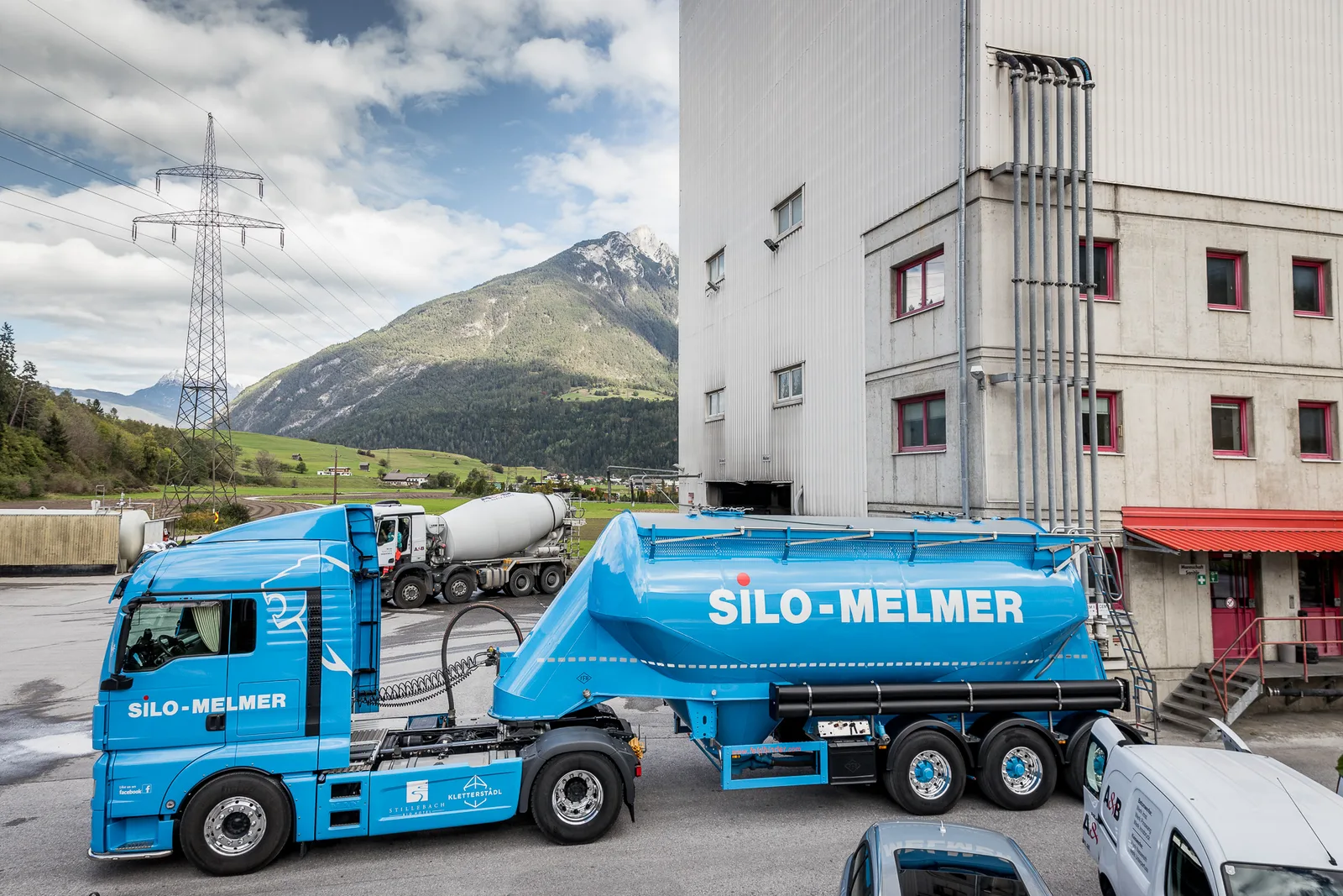Hellblauer Silozug mit Schriftzug SILO-MELMER vor einem Silo-Werk, im Hintergrund ein Berg