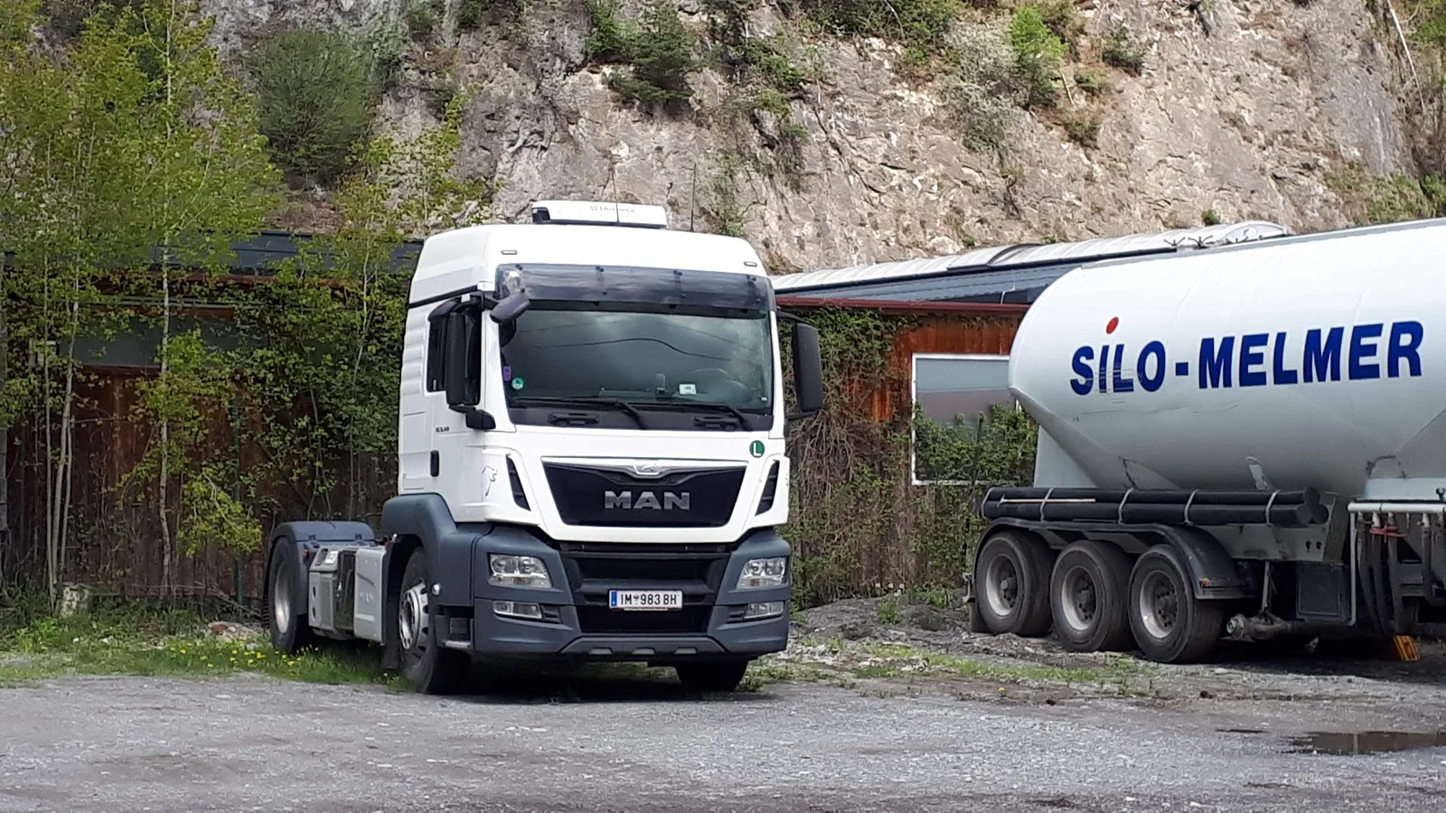 Weiße MAN-Zugmaschine neben einem Silo-Auflieger mit Schriftzug SILO-MELMER vor einer Felswand